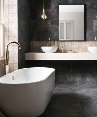 The black bathroom trend 2021 with black tiled wall and floor and white bath tub and sink.