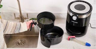 Person removing an air fryer basket beside a sink ready to clean