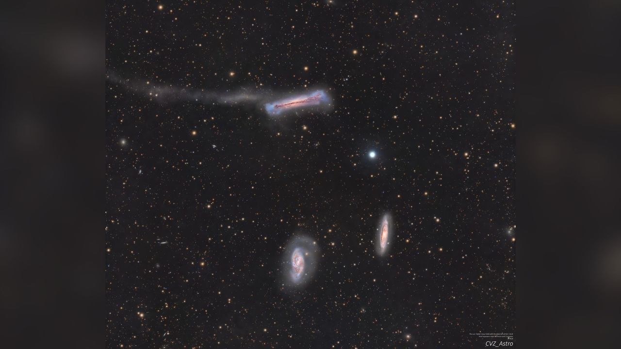 A trio of galaxies are pictured shining in deep space against a starfield dotted with more distant galaxies.