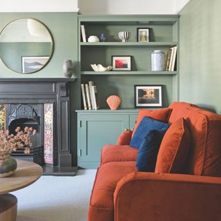 living room with green walls and built in storage an orange sofa and victorian fireplace