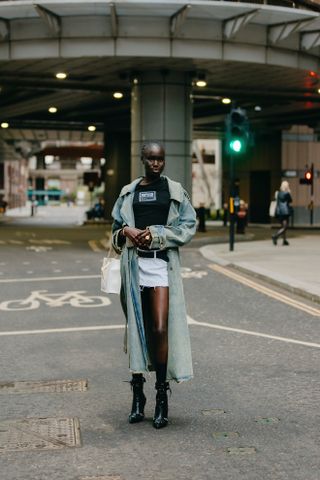 A woman wearing a white denim skirt, black tee shirt, blue denim jacket, platform heels.