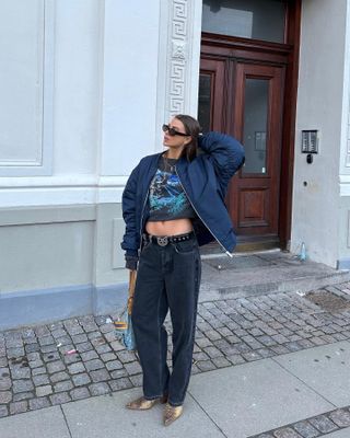 Woman wearing baggy jeans, crop top, ankle boots, and a bomber jacket