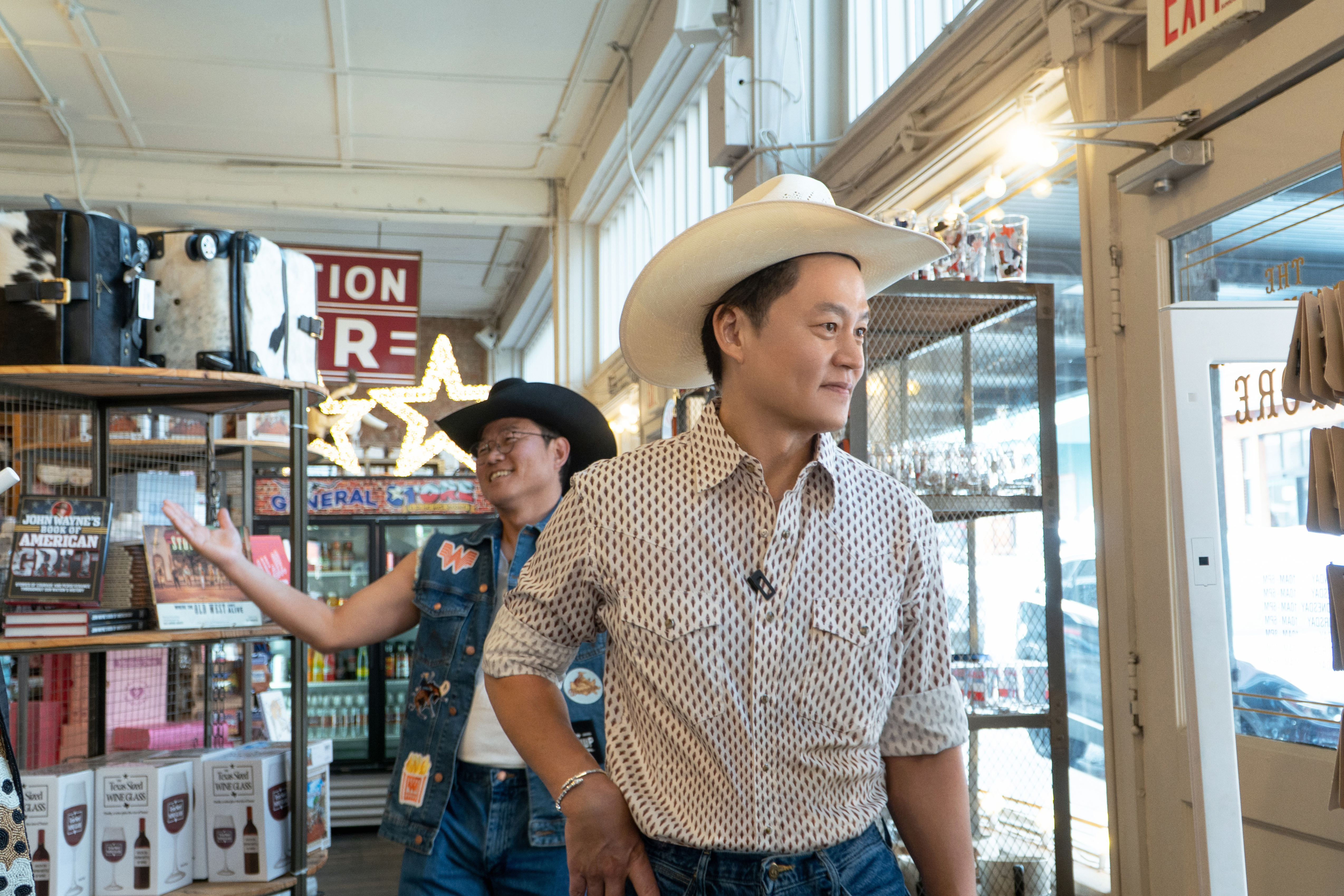 Two men wearing cowboy hats (l-r Na Young-seok, a.k.a. Na PD, and Lee Soo-jin) as they walk through a Texas gift shop, in Netflix's Korean reality show 'Ready or Not: Texas.'