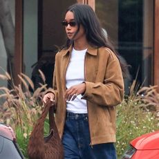 Laura Harrier smartens up dark wash baggy jeans with black leather loafers, a suede zip-up jacket and crisp white tee.