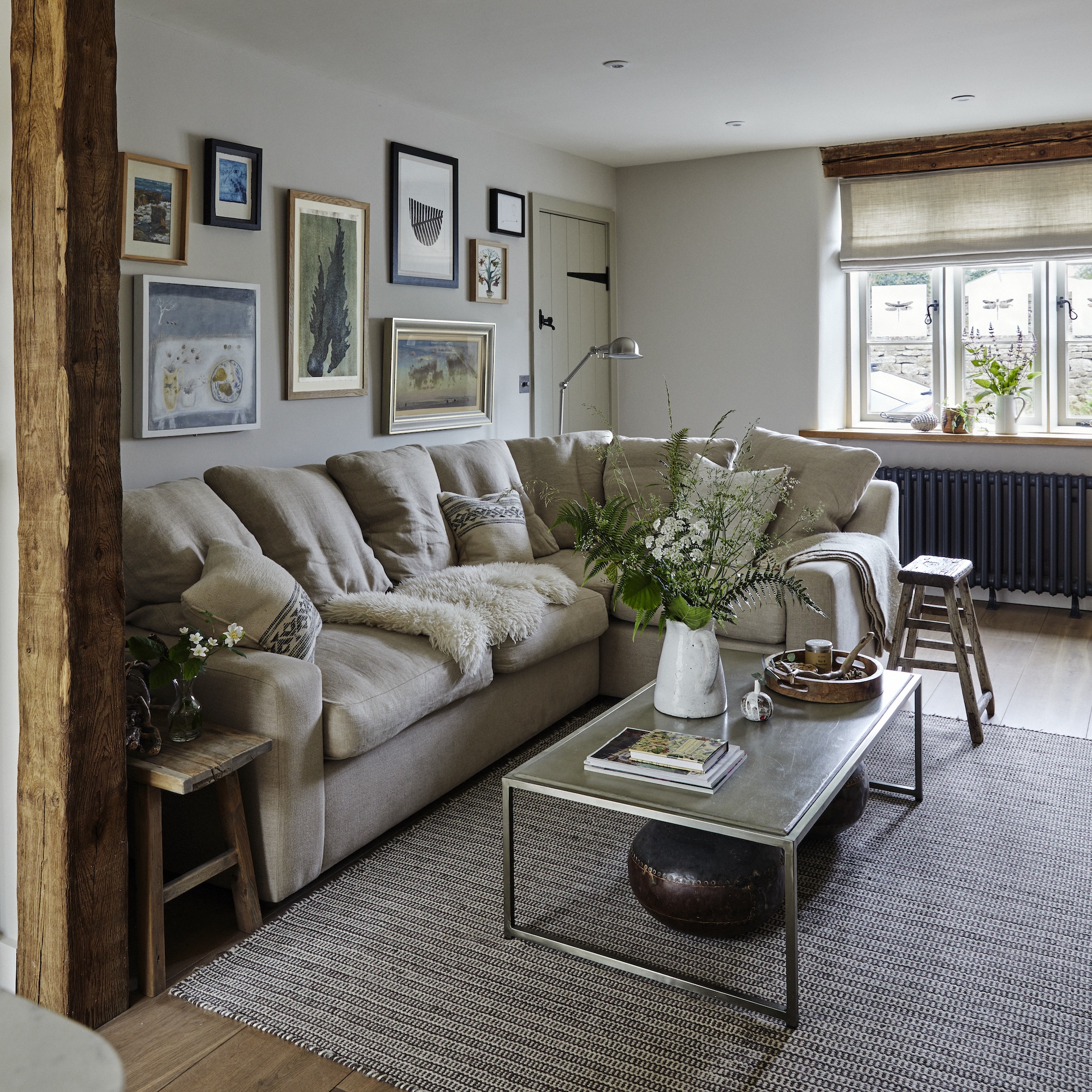 cottage sitting room with l-shaped cream sofa, coffee table on rug in centre of room and gallery wall of artworks behind sofa