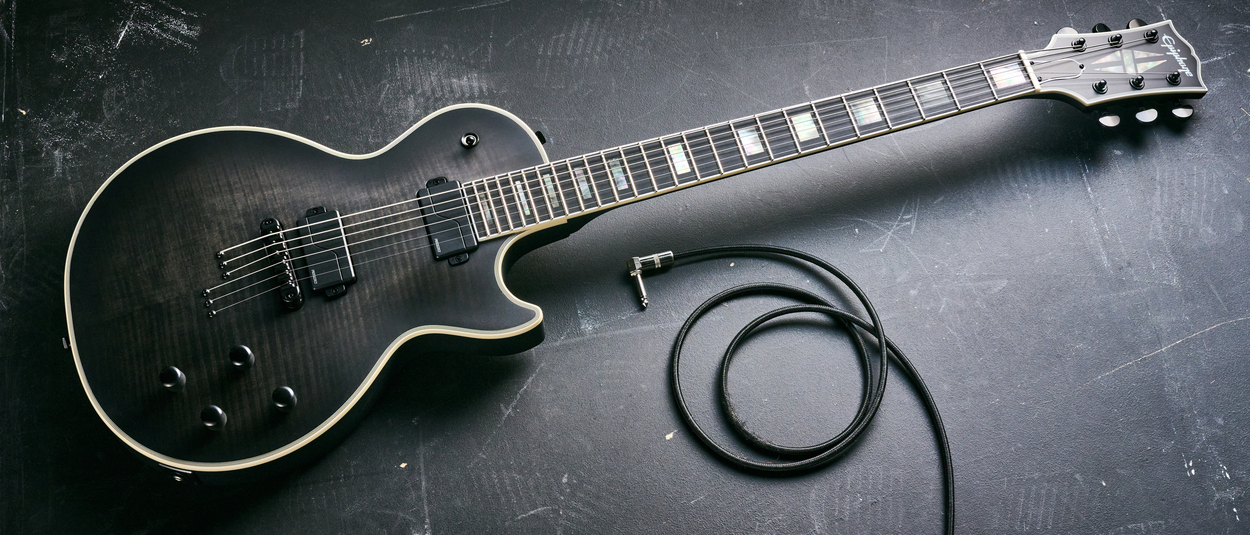 An Epiphone Prophecy Les Paul Baritone lying on a concrete floor with a guitar cable coiled nearby