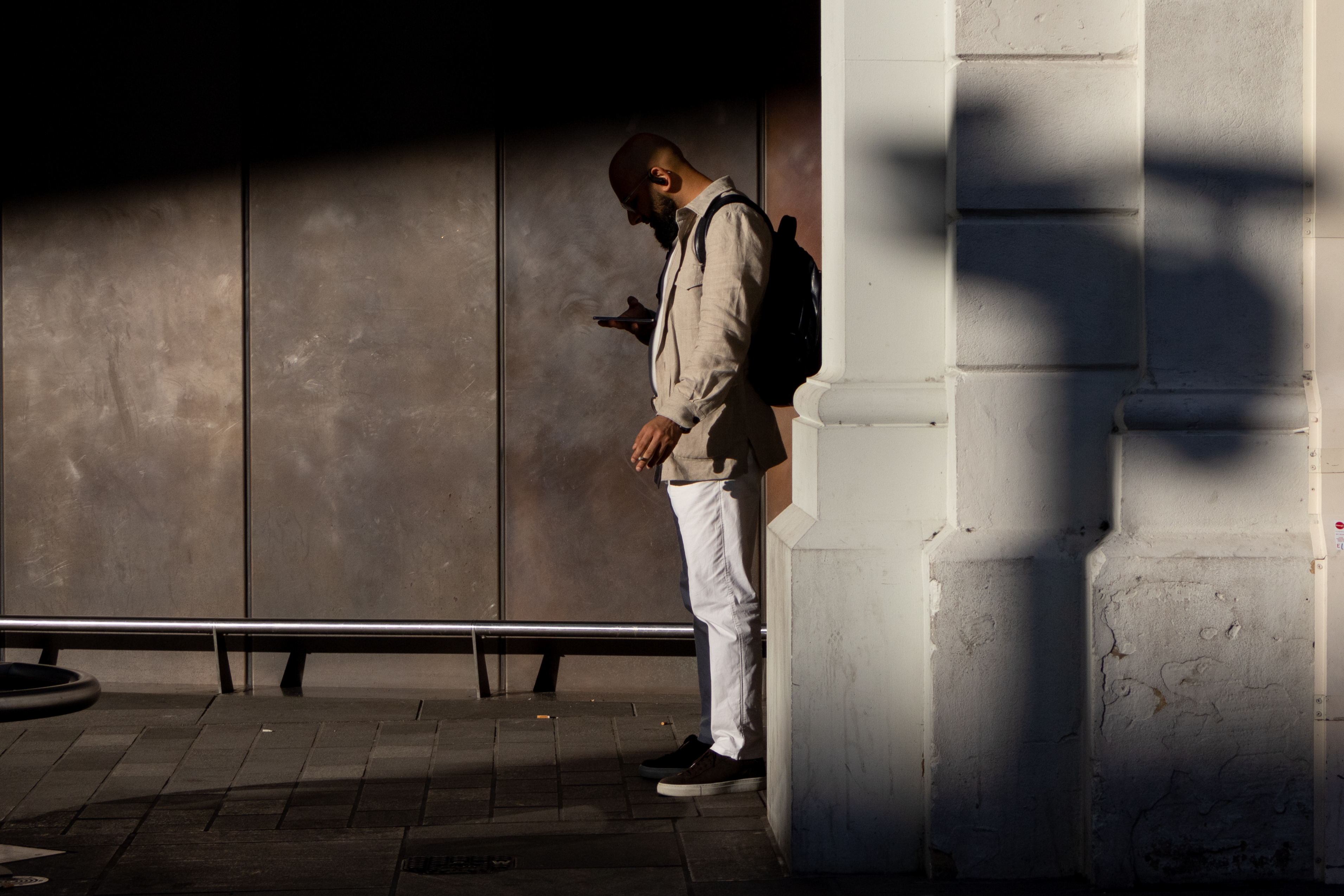 A man standing in the shade at a station reading his phone