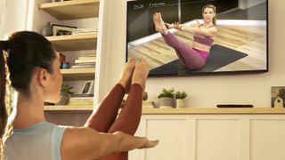 Peloton Digital review: A woman performs a yoga pose using the Peloton Digital app on her TV