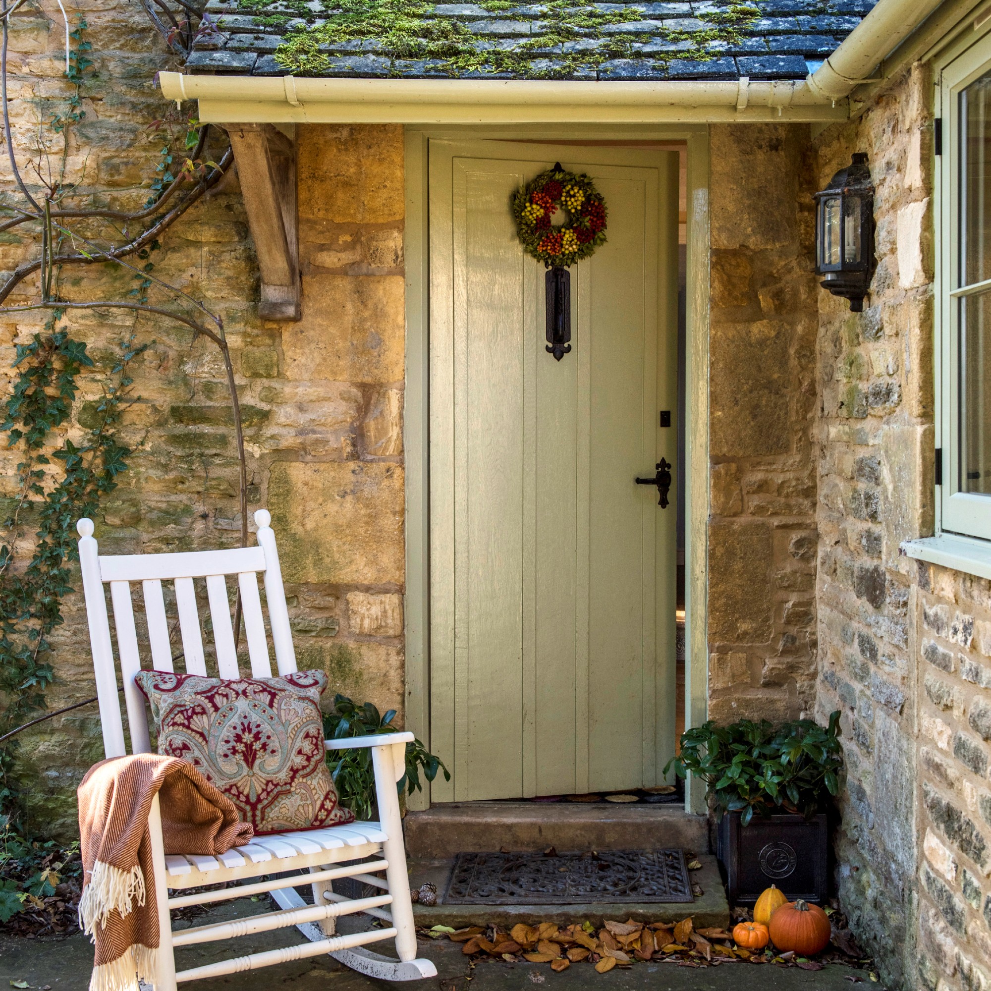 A front porch with a butter yellow front door adorned with a autumn-themed wreath and a rocking chair at front