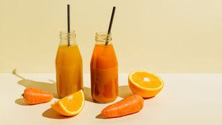 Milk-bottle-style glasses filled with fresh carrot juice and fresh orange juice