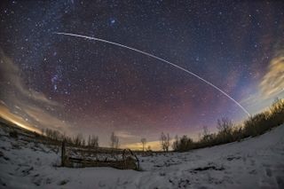 a streak of light passes overhead above a snowy winter scene full of stars