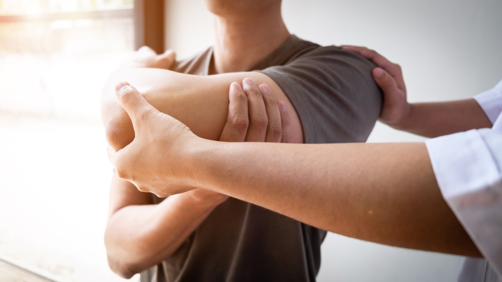 Mann mit Hand auf der Schulter während PNF-Dehnung, zweite Person hält seinen Ellbogen