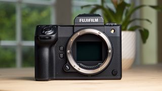 Front of the Fujifilm GFX100 II on a wooden table with viewfinder, but no lens attached