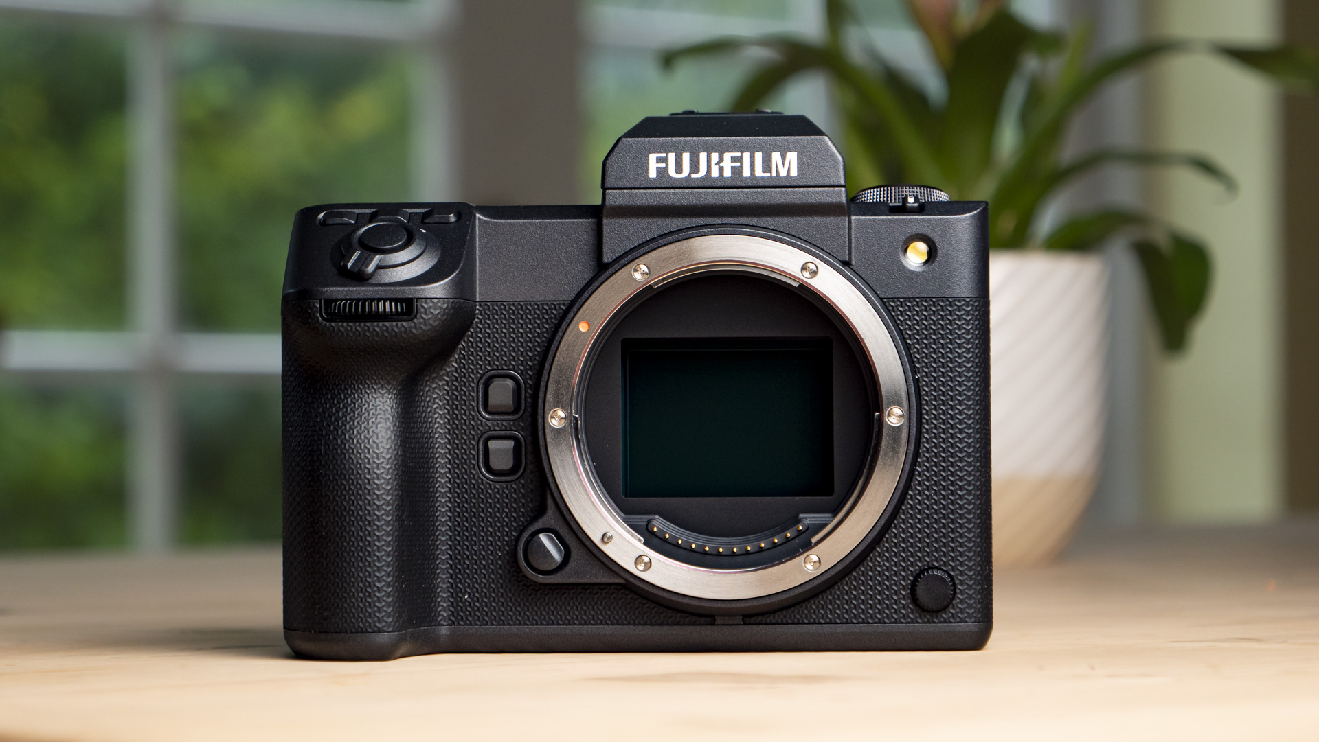 Front of the Fujifilm GFX100 II on a wooden table with viewfinder, but no lens attached 