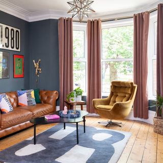 Blue living room with pink curtains at a bay window and a tan leather soaf