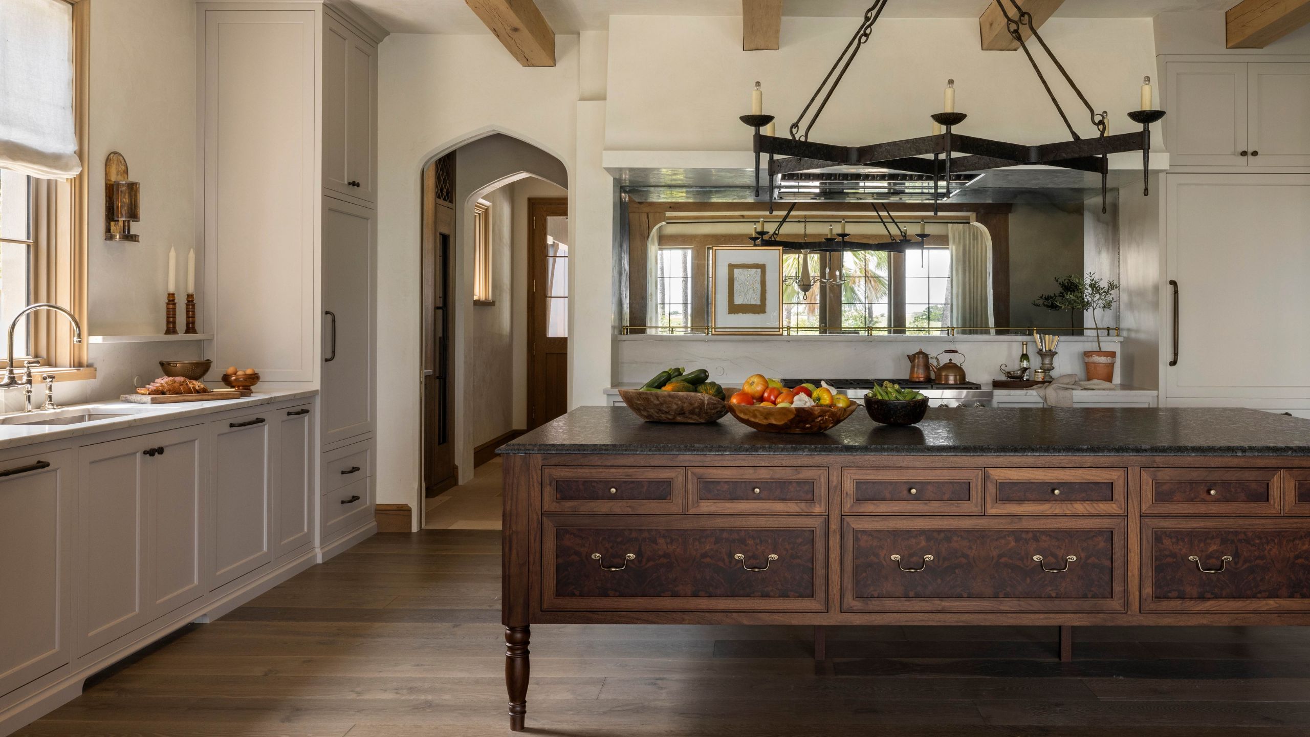 a rustic meets contemporary neutral kitchen with dark wooden antique style island, metal chandelier above and unique arched doorways