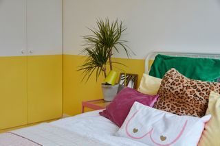 Bedroom with yellow and white colour block wall, mix of patterned cushions in green and pink