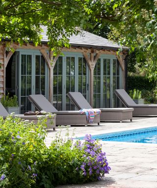 Pool house ideas with a Mediterranean style garden room and three pale gray sun loungers.