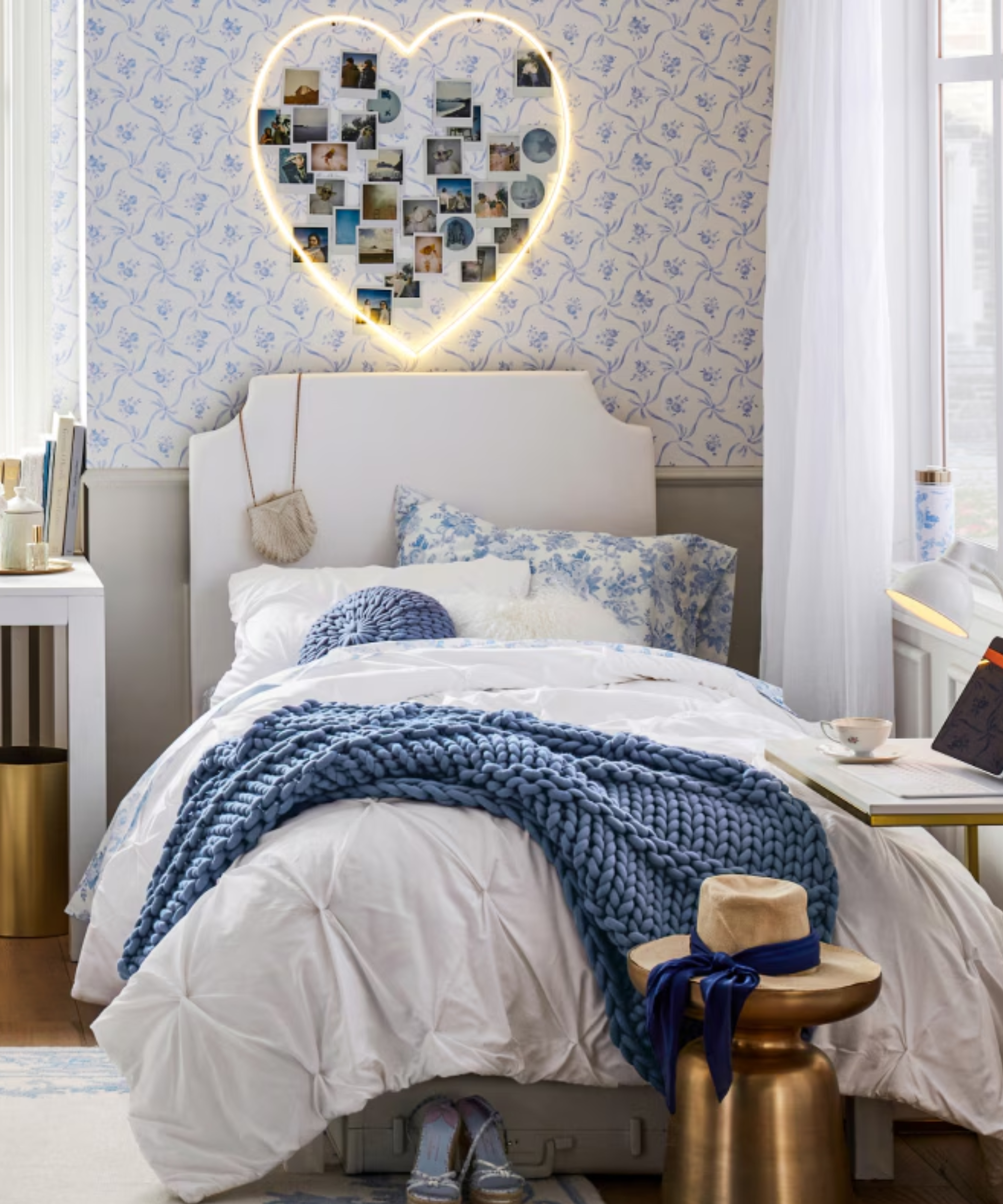 a dorm room with a twin bed with white and blue bedding and a heart light fixture hanging above the bed with pictures