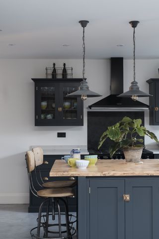 Kitchen with concrete floor, bespoke kitchen island in teal with wooden worktop and black factory-style pendant lamps.