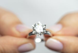 A close up of a woman holding a large diamond ring.