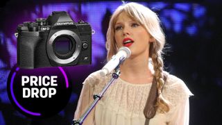 Taylor swift, wearing her hair in pigtails with a cream colored sweater, standing at a microphone, with an Olympus OM-D E-M10 Mark IV next to her and the text &quot;Price drop&quot;