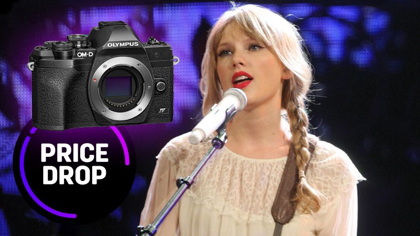 Taylor swift, wearing her hair in pigtails with a cream colored sweater, standing at a microphone, with an Olympus OM-D E-M10 Mark IV next to her and the text &quot;Price drop&quot;