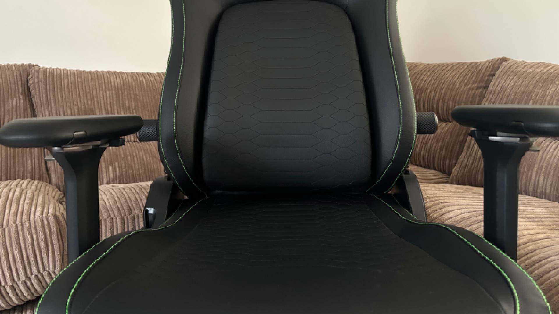 Razer Iskur V2 NewGen gaming chair seat and backrest showing embroidered snake pattern and arm rests with a brown sofa in the background with a white wall.