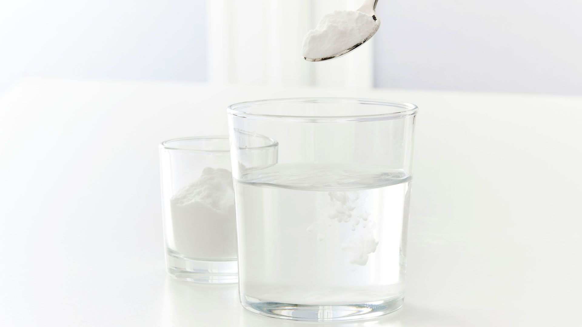 Glass of water with a teaspoon of baking soda being added as a drink to master how to keep a Christmas tree alive for longer