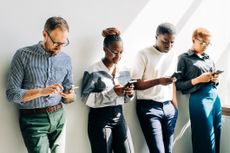 Four people leaning against a wall looking at their pension pots on their phones considering pension consolidation