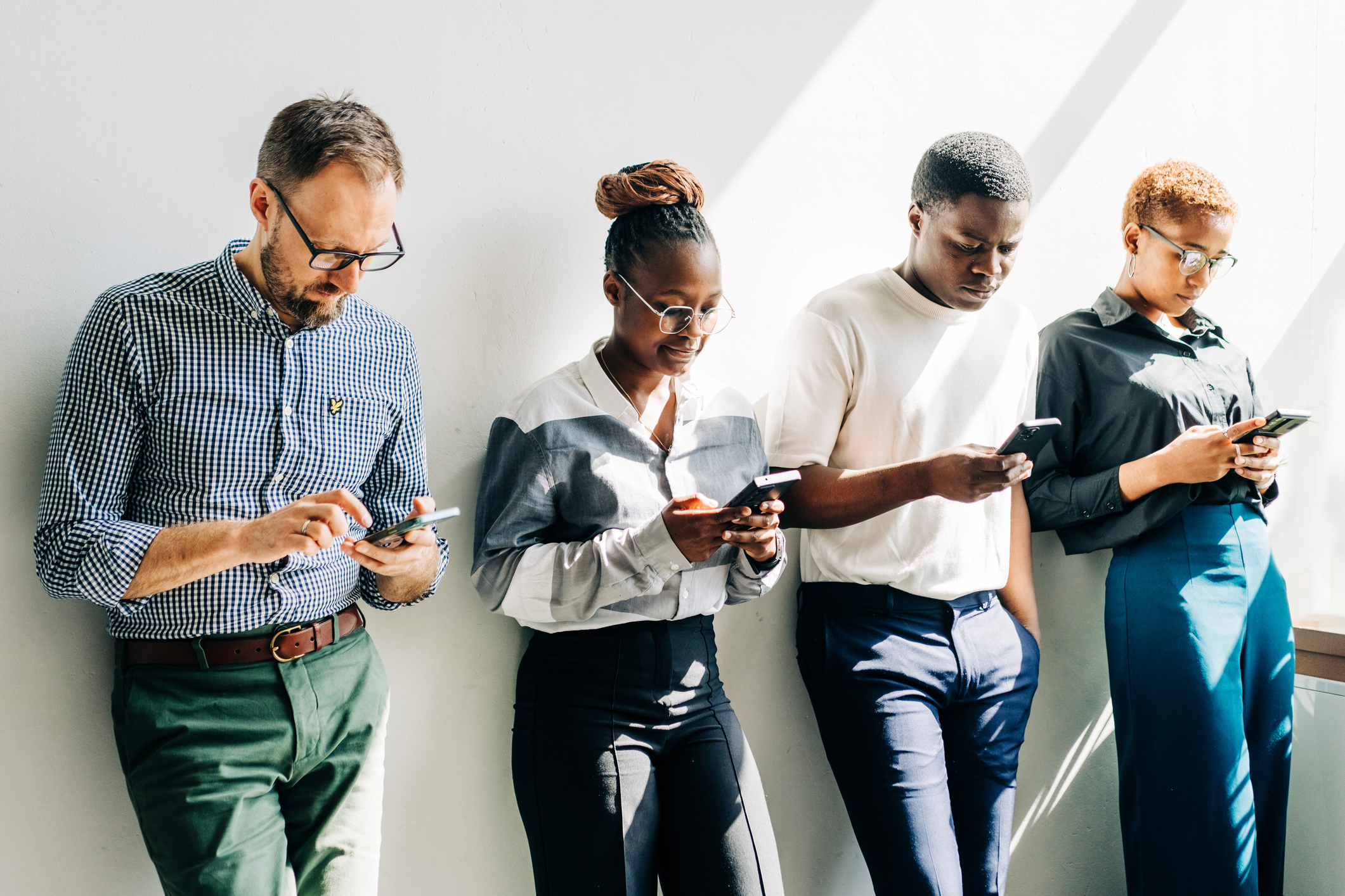Four people leaning against a wall looking at their pension pots on their phones considering pension consolidation