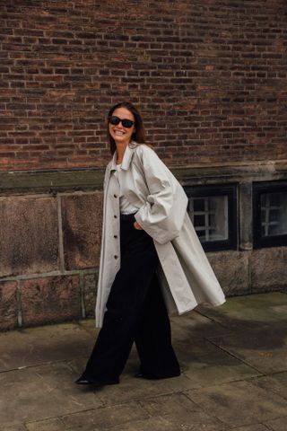 A woman wearing black pants, a white tee, and a fall trench coat.