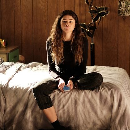 a woman (zendaya as rue) sits on a bed while holding a phone, in 'euphoria' season 2