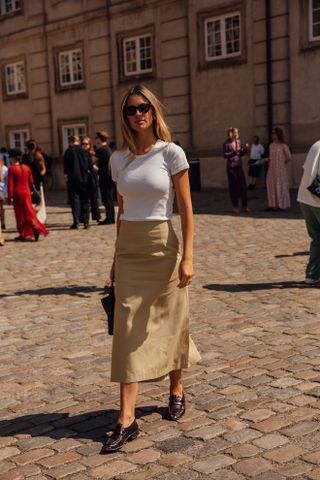 A guest attends the Copenhagen spring summer 2025 fashion week shows in a white t-shirt, khaki midi skirt, and driver loafers