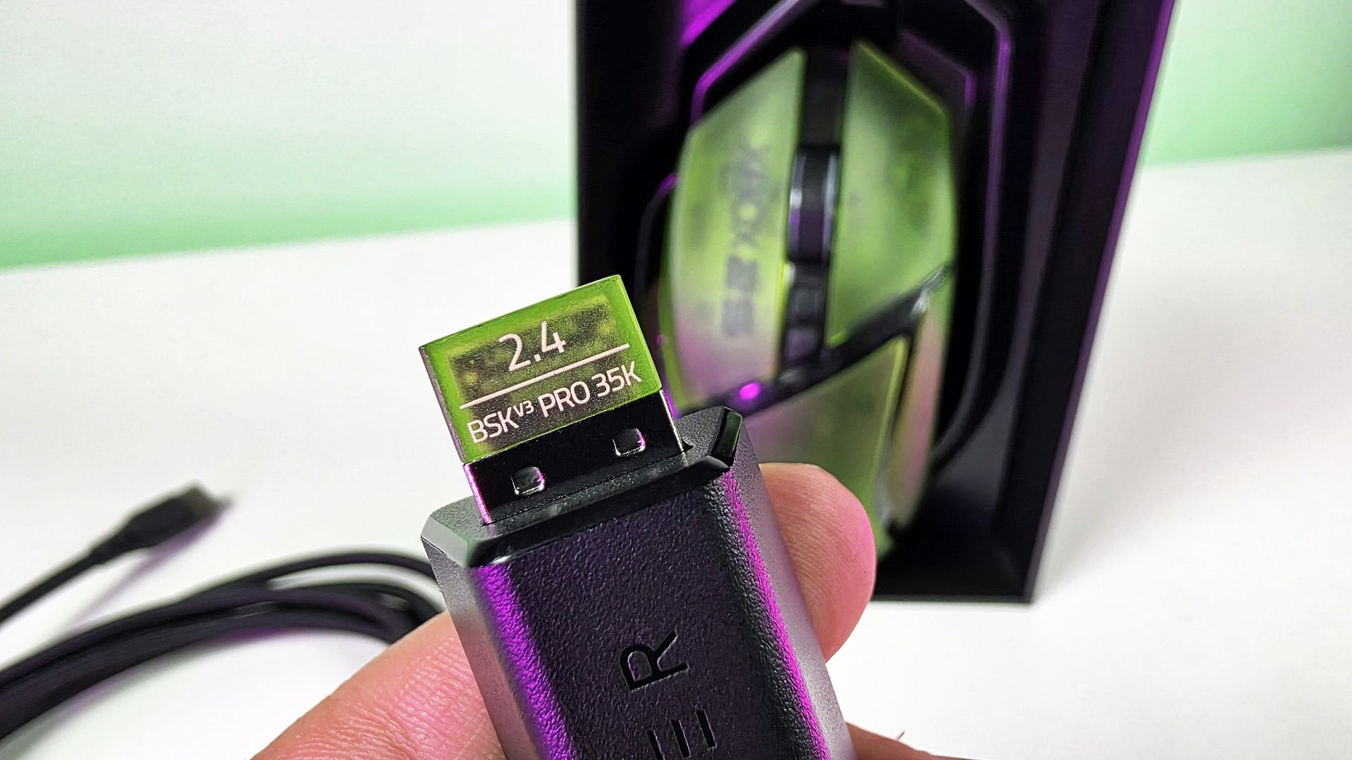 Close-up of the Razer Basilisk V3 Pro 35K 2.4 GHz USB wireless dongle in translucent green plugged into an adapter, with the mouse and packaging in the background