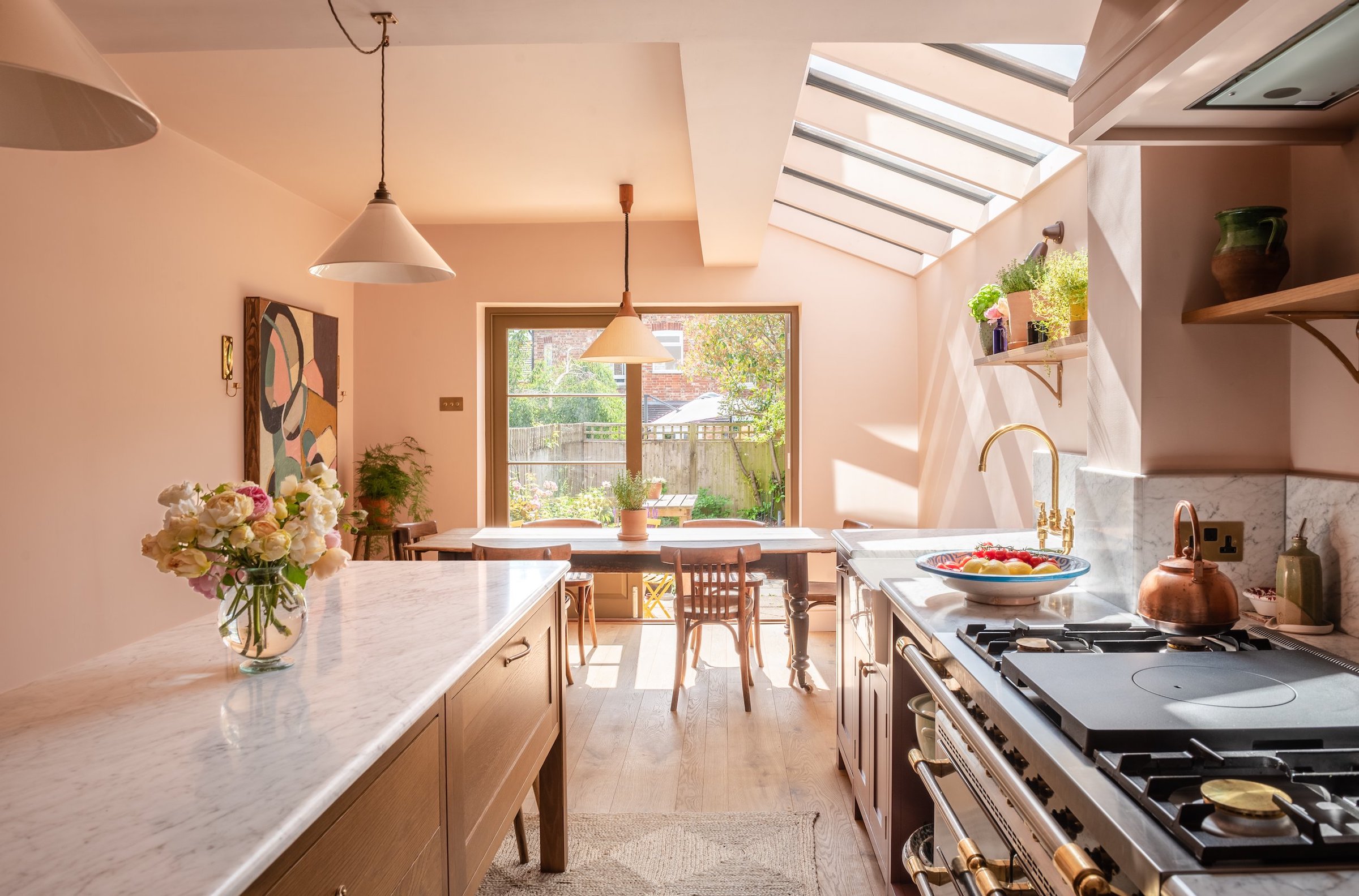 pink side return extension with a dining table in the space. There is a plant on the dining table. The kitchen has large doors with a view of the backyard.