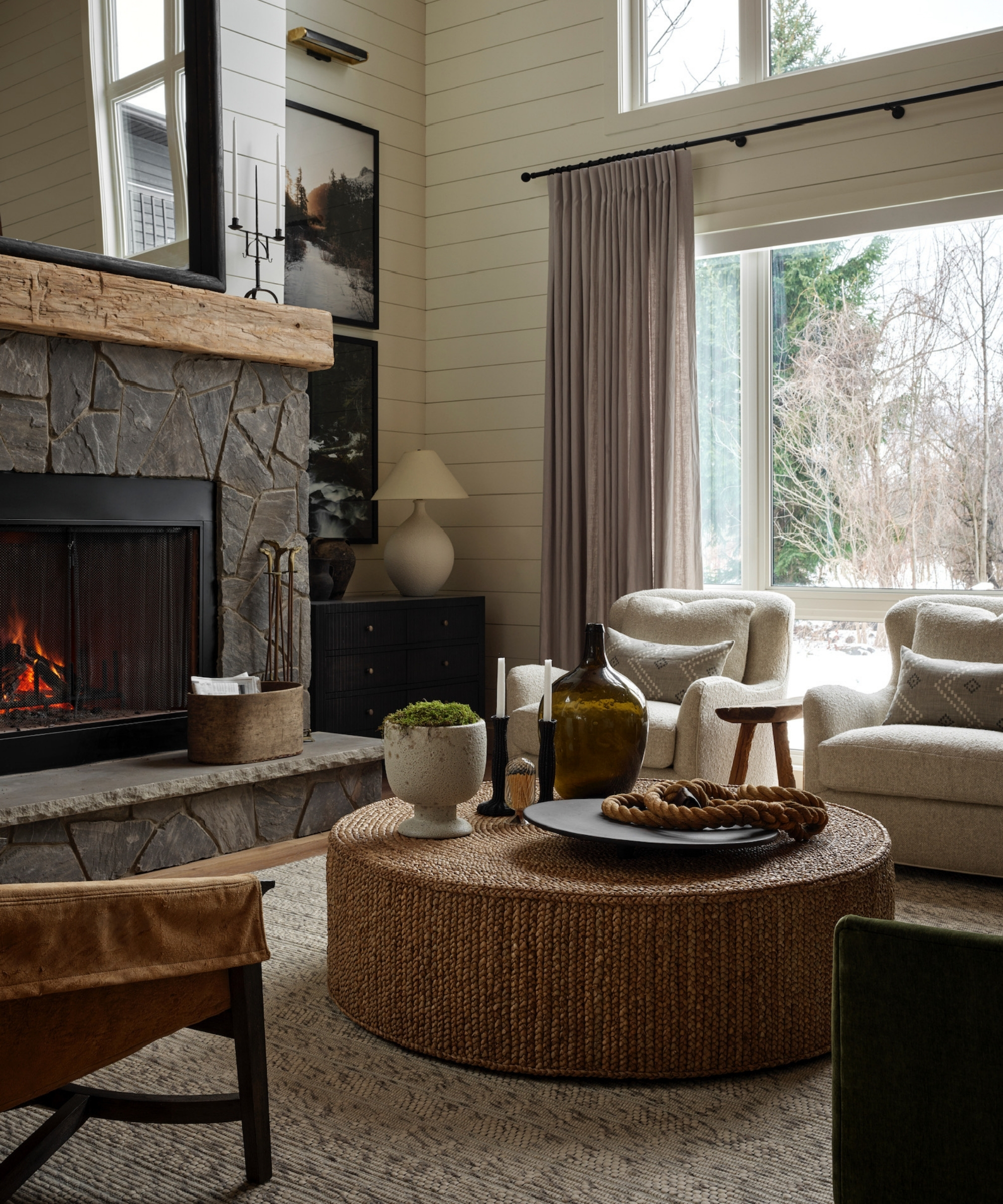 Living room with stone fireplace, woven coffee table, layered seating, candlesticks, ceramics and decorative objects.