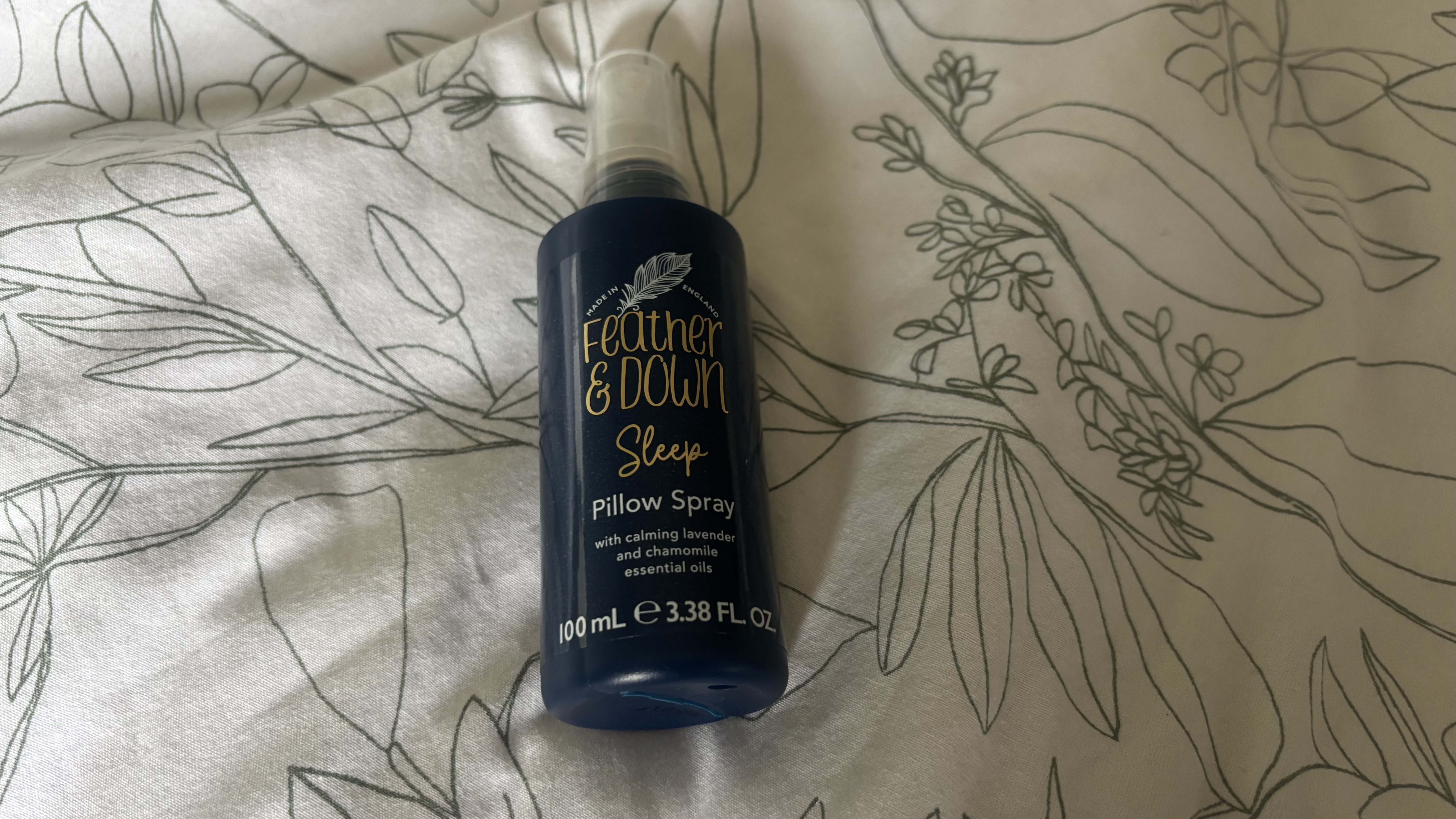 A bottle of Feather & Down Pillow Spray on a bedspread.