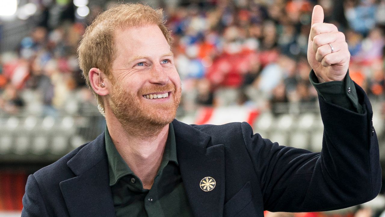 Prince Harry wearing a suit jacket and green shirt and looking up and smiling giving a thumbs up