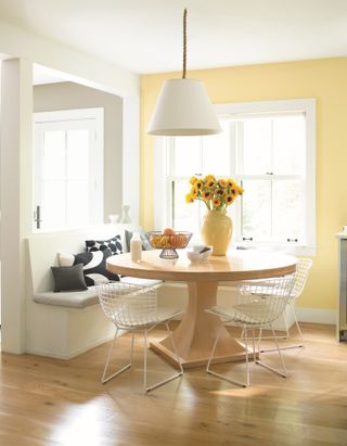 A bright dining room with a round wooden table and one yellow wall combined with a beige wall.