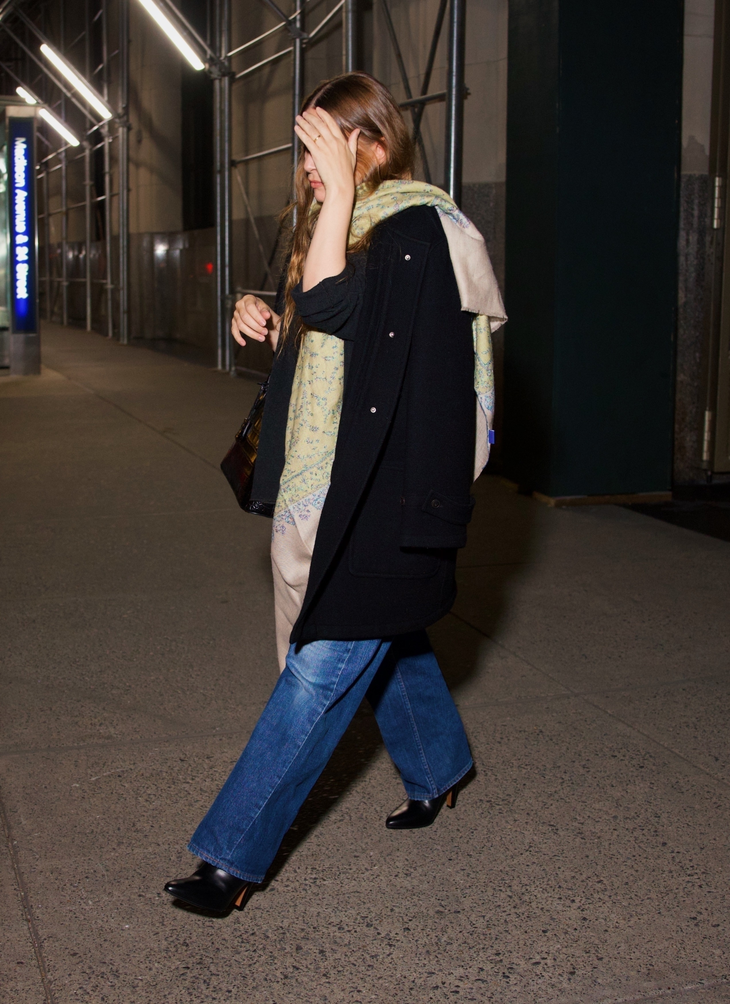 An image of Ashley Olsen wearing a black coat with a shawl, blue jeans and black boots.
