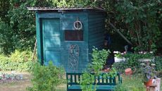 A small green shed and green bench sit aside a vegetable garden