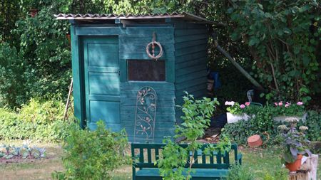 A small green shed and green bench sit aside a vegetable garden