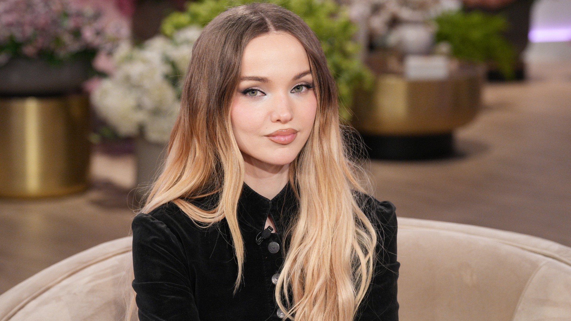 a white woman with dark roots and blonde ends posing on a set in front of a studio audience