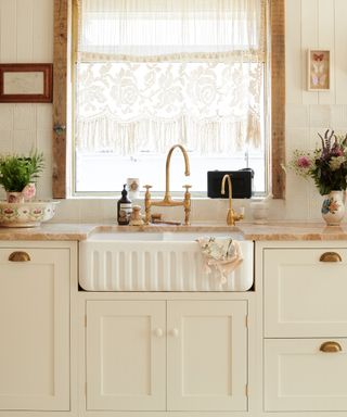 drapes vs blinds, cream vintage style kitchen with butler sink, lace cafe curtain at window, marble countertop, shiplap walls, brass faucet