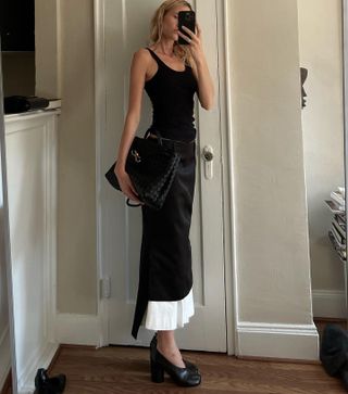 Elly McGaw wearing a black tank top, black-and-white layered Sportmax skirt, black heels, and a black Bottega Veneta Andiamo bag.