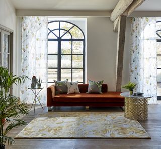 Sheer curtains featuring subtle botanical design in a living room with floral rug and chaise style terracotta sofa.