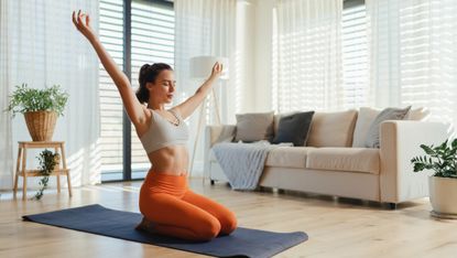 Woman kneeling on a yoga mat with arms above head