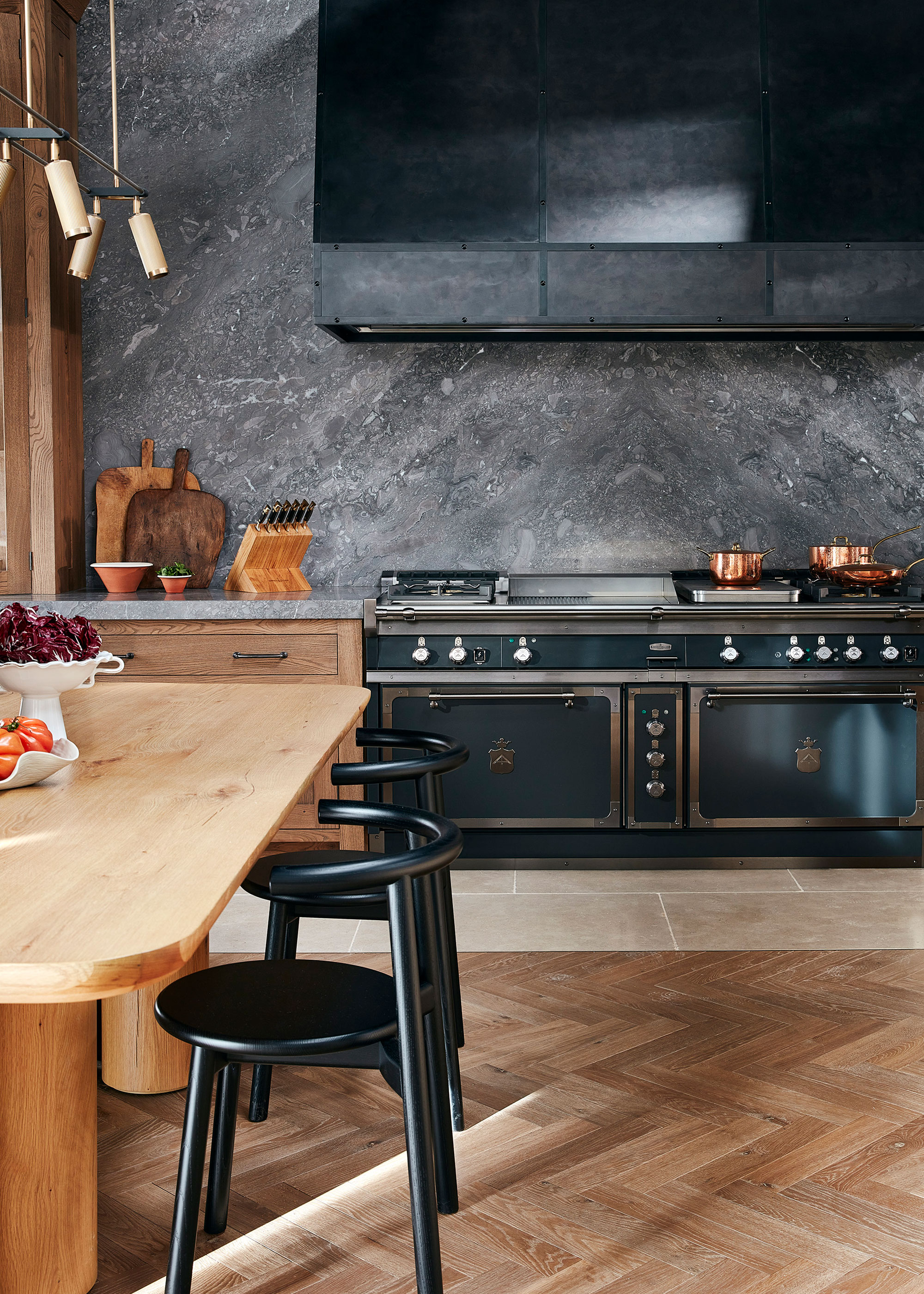 wooden kitchen with stone full height backsplash and large black range cooker with wooden herringbone flooring
