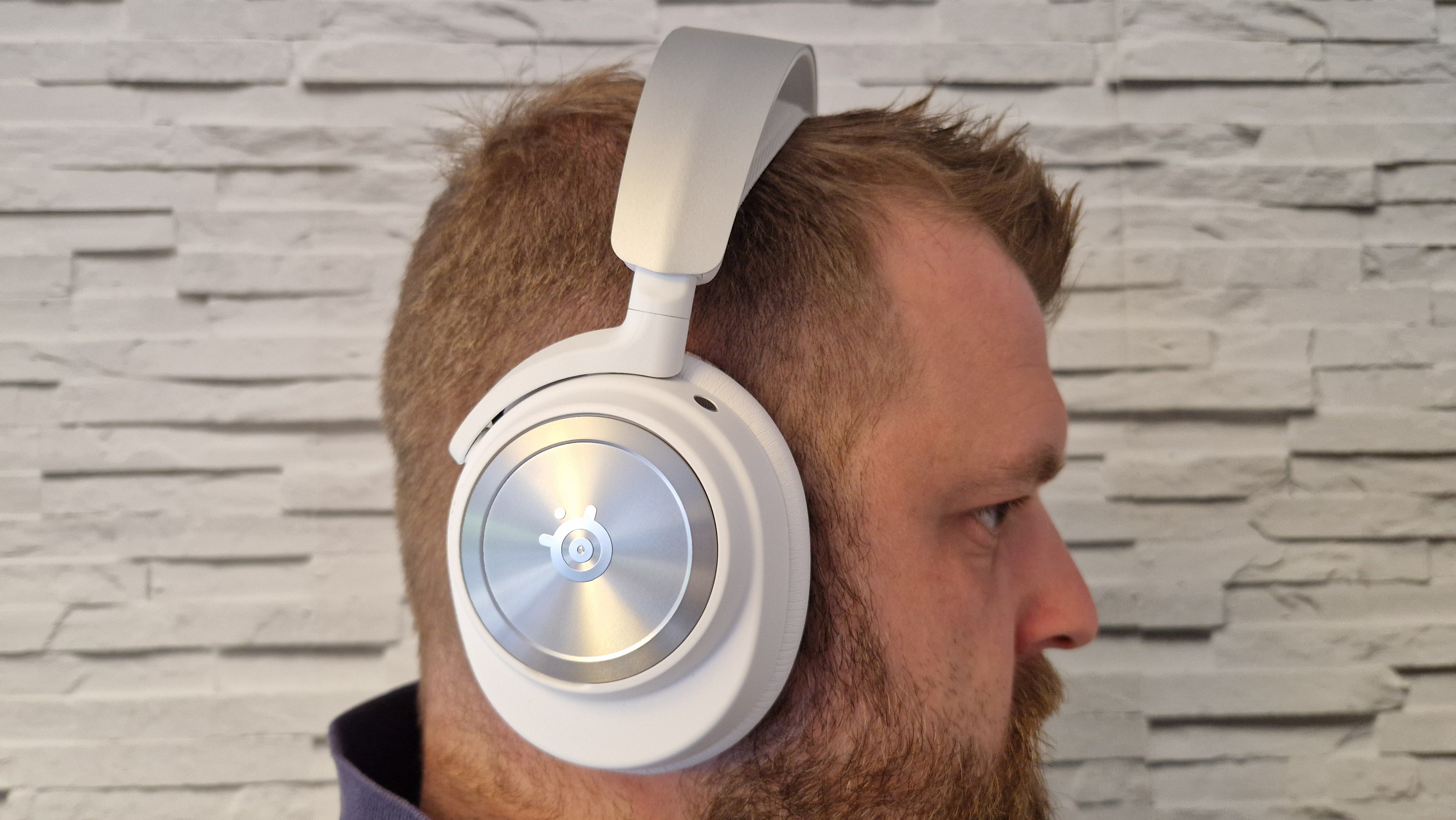 The SteelSeries Arctis Nova Pro Wireless white edition on a user's head with a white brick background